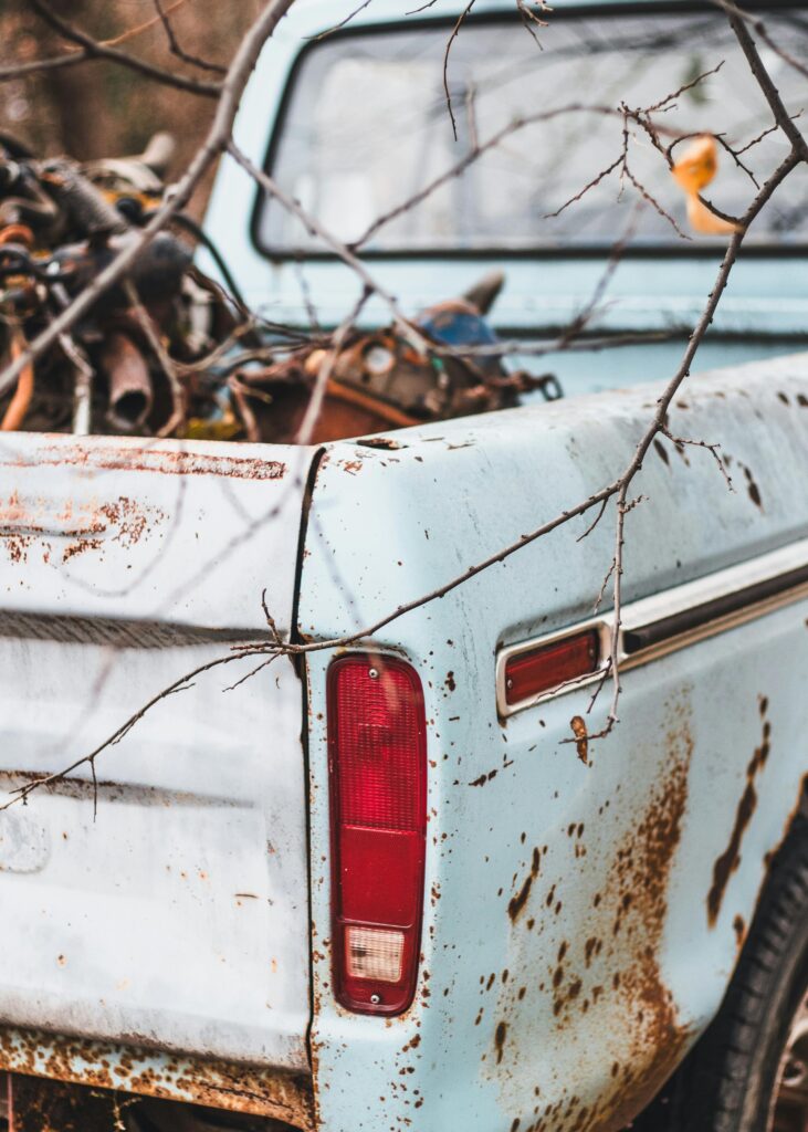 Close-up of a rusty vintage pickup truck's taillight and rear, surrounded by autumn branches.